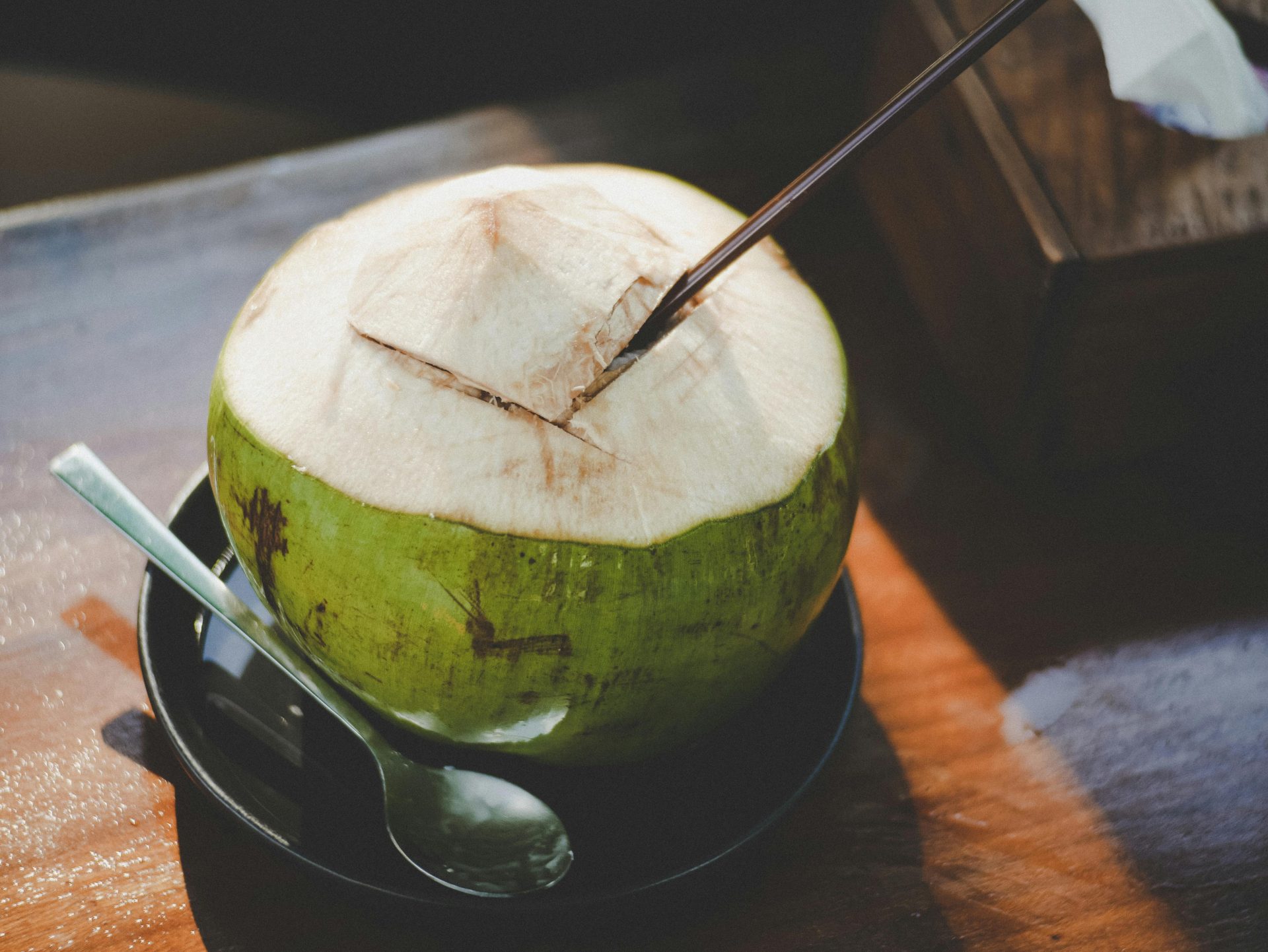 A close-up of a fresh coconut with a straw and spoon, beautifully captured indoors.